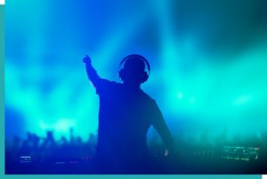 DJ mit Equipment vor tanzendem Publikum mit grüner und blauer Lichttechnik